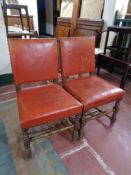 A pair of early 20th century oak dining chairs upholstered in a red studded leather