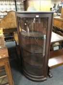 An antique stained pine bow front glazed corner cabinet