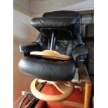 A contemporary black leather swivel adjustable armchair with matching footstool