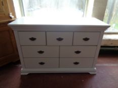 A contemporary white seven drawer chest with metal drop handles