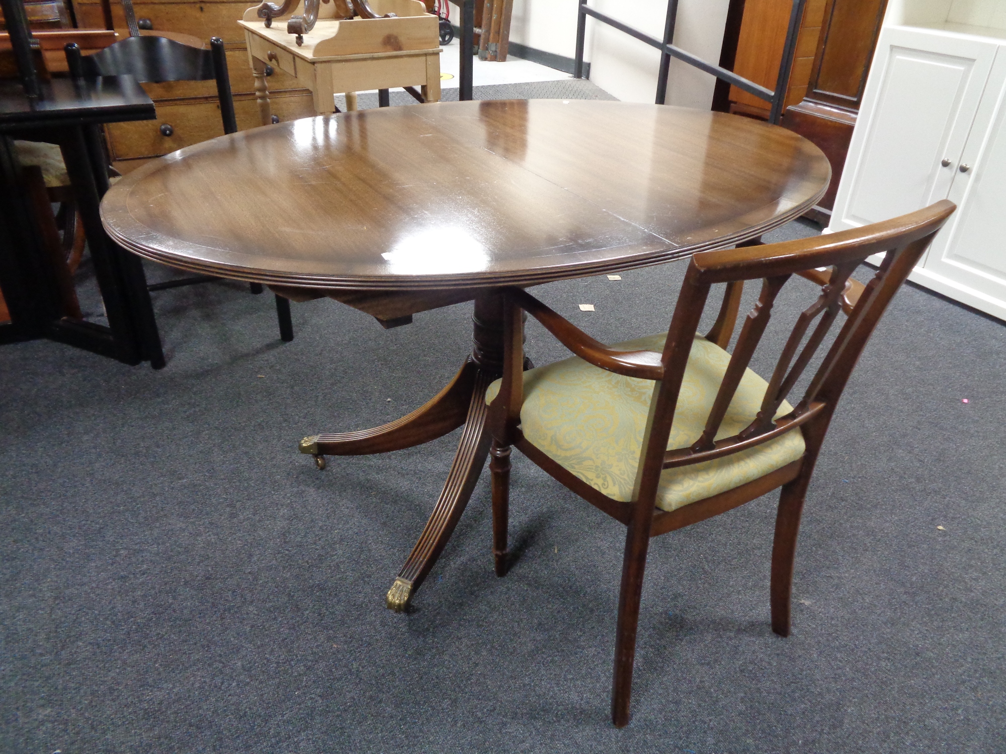 An oval inlaid mahogany pedestal dining table with leaf and a mahogany armchair