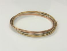 A tri-colour 9ct gold bangle with hinge clasp,