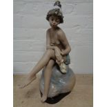 A large Spanish (Lladro?) figure of a nude female seated on rock on wooden stand, height 47 cm.