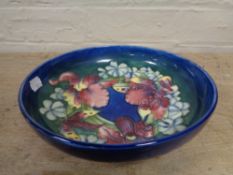 A W Moorcroft shallow bowl decorated with orchids on blue ground,