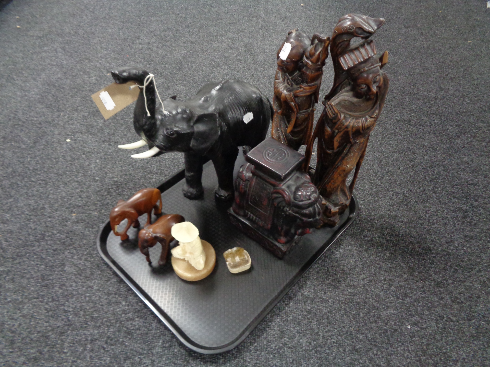 A tray of two carved hardwood figures, leather elephant,