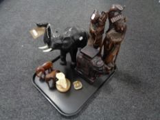 A tray of two carved hardwood figures, leather elephant,