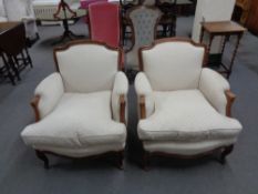 A pair of carved beech framed French style armchairs in cream fabric