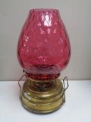 An antique brass paraffin lamp with cranberry glass shade