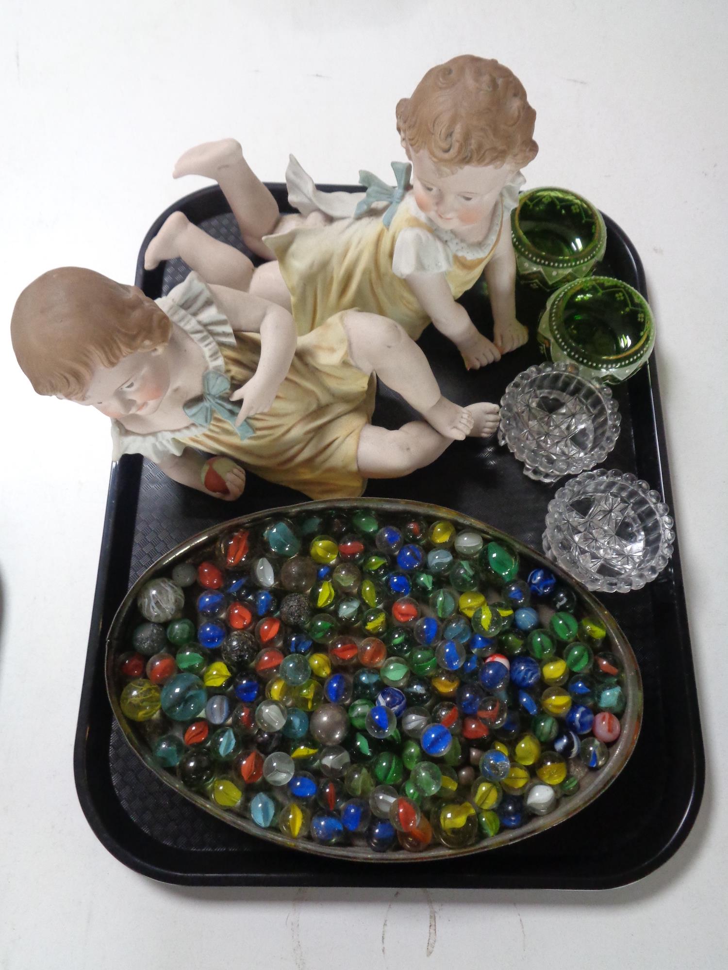 A tray containing a tin of assorted glass marbles, two bisque figures of children,