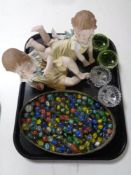 A tray containing a tin of assorted glass marbles, two bisque figures of children,