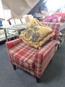 An armchair upholstered in a red checked fabric together with a tasselled cushion depicting a coat