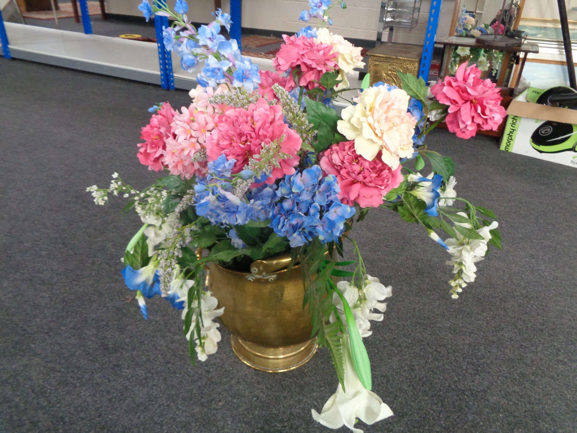 A large antique brass coal bucket containing artificial flowers