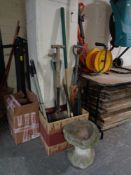 A box of assorted garden tools and a hand saw together with a stone bird bath