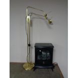 An electric heater in the form of a stove, together with a brass angle poise floor lamp.