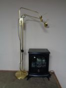 An electric heater in the form of a stove, together with a brass angle poise floor lamp.