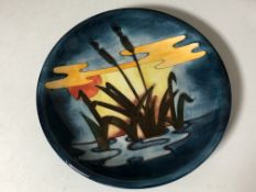 A modern Moorcroft plate depicting bulrushes at sunset.