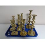 A tray containing a pair of antique brass candlesticks together with six further brass candlesticks.