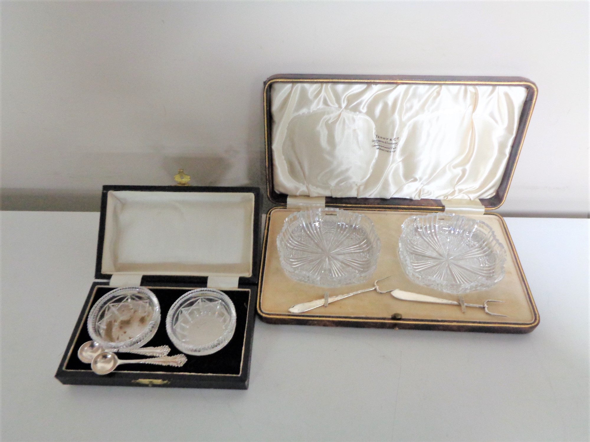 A case set of cut glass salts with silver spoons together with a further case set of cut glass