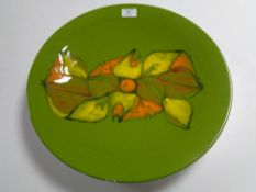 A large Poole Pottery circular plaque, olive green with abstract orange and yellow decoration,