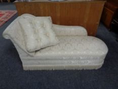 A chaise longue upholstered in a cream brocade fabric together with matching cushion.