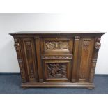 A 20th century profusely carved oak triple door cocktail sideboard on bun feet.