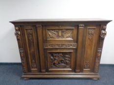 A 20th century profusely carved oak triple door cocktail sideboard on bun feet.