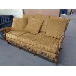 An antique carved bergere three seater settee upholstered in a gold stripe fabric with gold