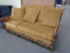 An antique carved bergere three seater settee upholstered in a gold stripe fabric with gold