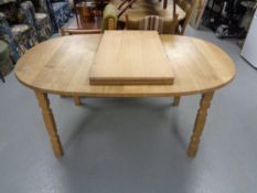 An oval blond oak extending dining table with two leaves