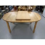 An oval blond oak extending dining table with two leaves