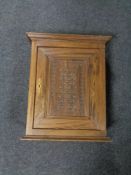 An antique oak wall cabinet with a carved panel door.