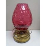 An antique brass paraffin lamp with cranberry glass shade