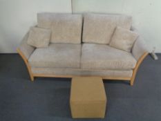 A wooden framed two seater settee in beige fabric together with a foot cube