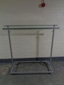 A metal adjustable shop clothes rail with glass shelf