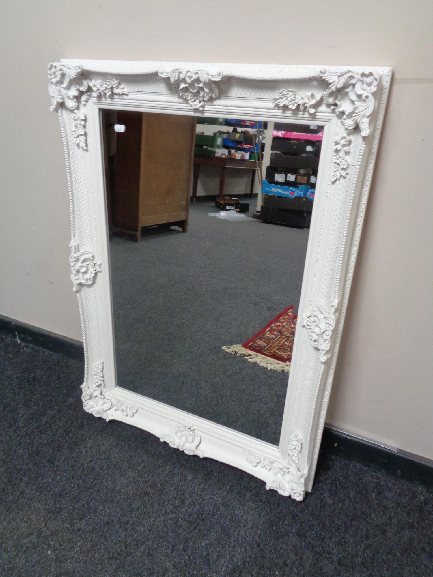 A white ornate painted framed bevel edged mirror.