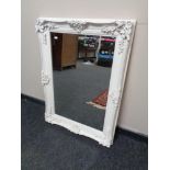 A white ornate painted framed bevel edged mirror.