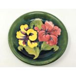 A Walter Moorcroft 'Hibiscus' pattern plate on green ground, Queen Mary Label, diameter 22cm.