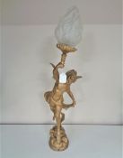 An antique painted spelter table lamp with shade modelled as a winged boy bearing a torch