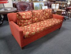 A three seater settee upholstered in a red floral fabric.