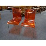 A pair of Italian orange perspex dining chairs on metal legs.