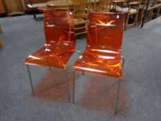 A pair of Italian orange perspex dining chairs on metal legs.