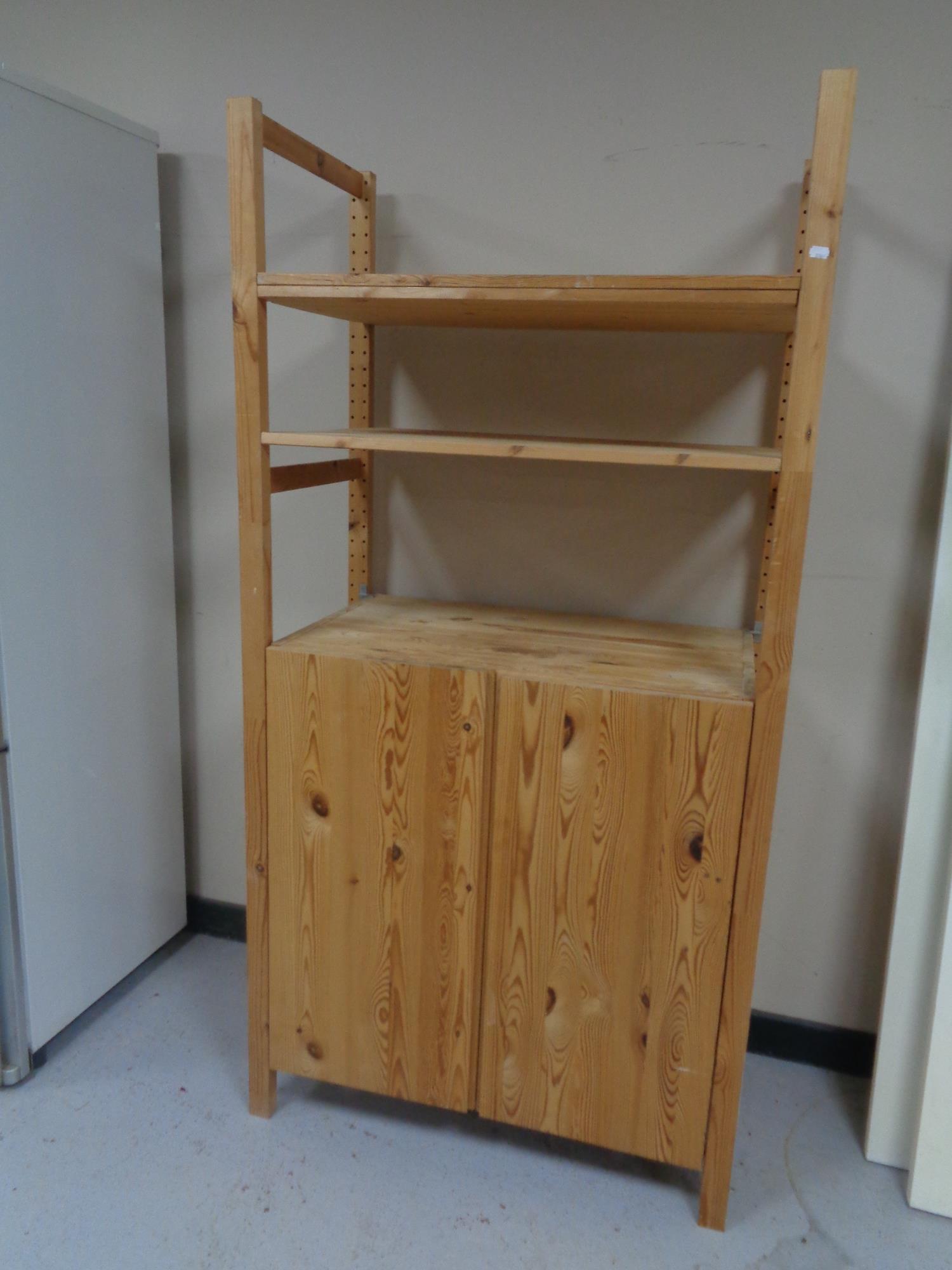 A set of Ikea stripped pine open bookshelves, fitted cupboard below.