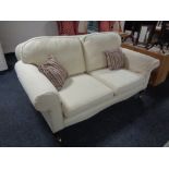 A Victorian style two seater settee upholstered in a cream fabric.