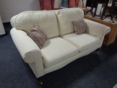 A Victorian style two seater settee upholstered in a cream fabric.