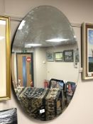 An oval all glass bevelled mirror, 61 cm x 89 cm.