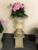 A composition stone campana urn on stand planted with Dahlias,