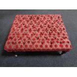 An oversized foot stool re-upholstered in a red and cream fabric on ceramic casters.