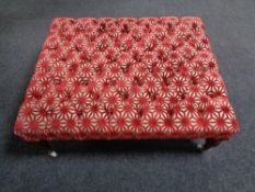 An oversized foot stool re-upholstered in a red and cream fabric on ceramic casters.