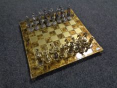 A brass topped chess board on raised feet together with metal Roman chess pieces.