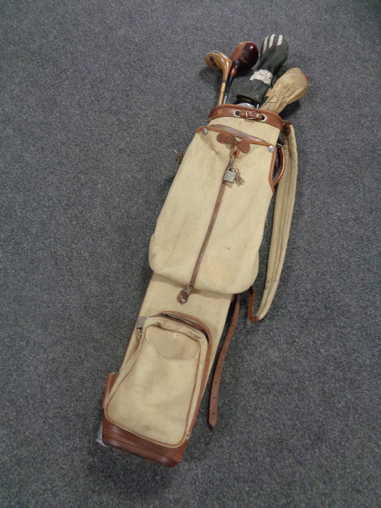 A vintage canvas golf bag containing five vintage drivers and two irons.